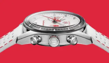 Side view of a TAG Heuer Carrera chronograph watch with a white dial, red accents, and a white perforated strap on a red background.