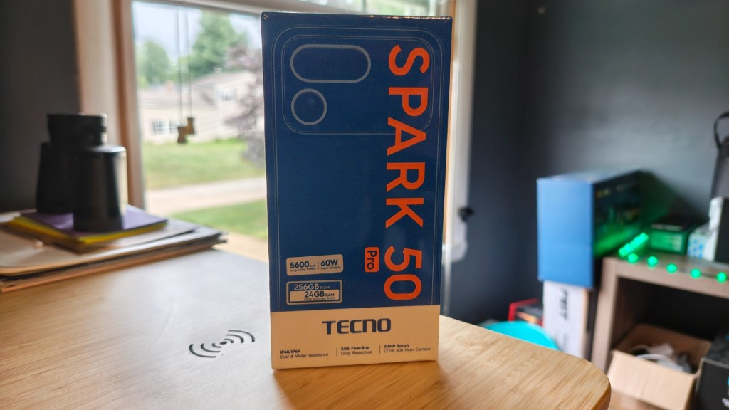 TECNO Spark 50 Pro smartphone box with specifications, including 256GB storage and 24GB RAM, placed on a wooden surface near a window.