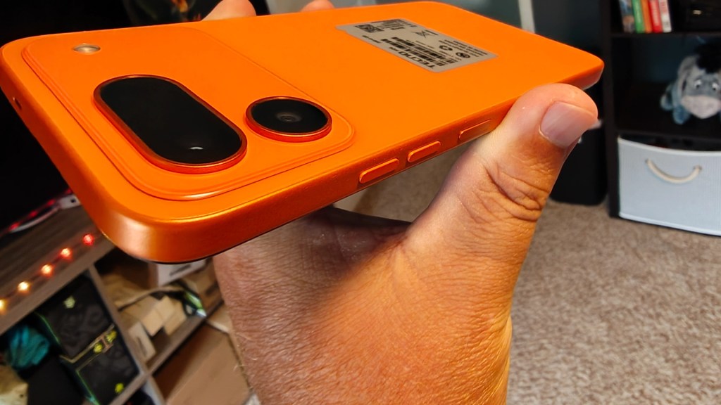 A person holding a bright orange smartphone from the side, showcasing the camera and button placements.