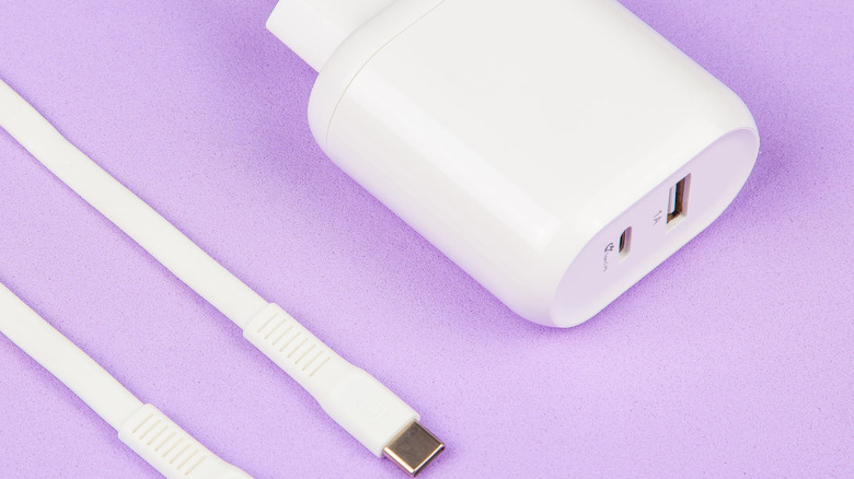 A white dual-port wall charger resting next to two white charging cables on a pink backdrop.
