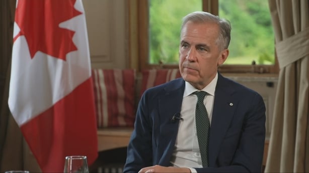 Mark Carney sits in front a Canadian flag.