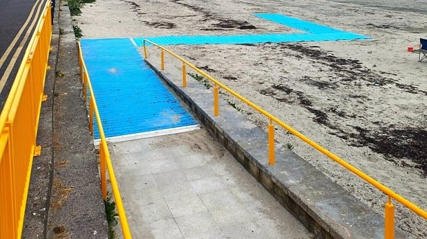 A ramp leads down to a blue accessible beach map on a beach