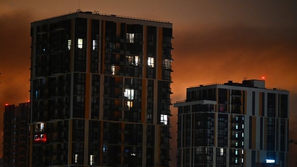The photograph shows a glow behind urban buildings during an explosion following massive Russian ballistic missile strikes in the Ukrainian capital of Kyiv on August 1, 2026