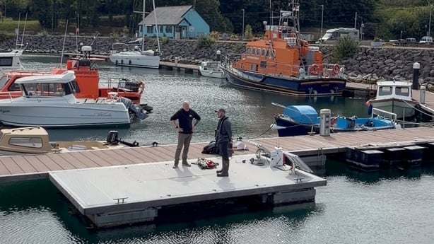 Two men standing on a jetty beside a floating oyster reef