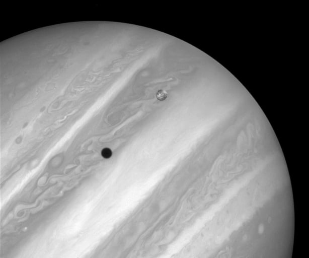 This image, shows Jupiter's volcanic moon Io passing above the turbulent clouds of the giant planet, on July 24, 1996. The conspicuous black spot on Jupiter is Io's shadow. The smallest details visible on Io and Jupiter are about 100 miles across (about 160 kilometres). Bright patches visible on Io 