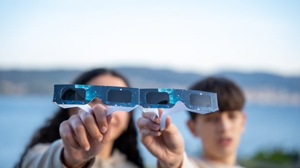 Adolescents holding and showing protective solar eclipse glasses to the camera outdoors. Concept of safety and science education.