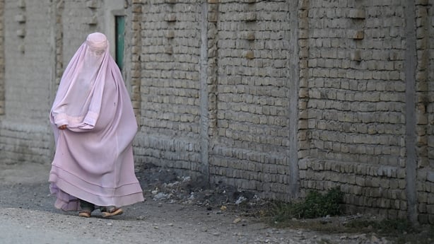 a burqa-clad woman walks along a street