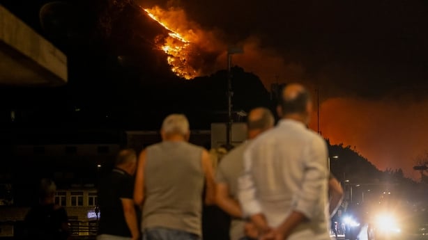 Bystanders watch as a wooden area is engulfed in flames during a raging wildfire near the town of Omis, some 30 kilometres south of Split on August 14, 2026