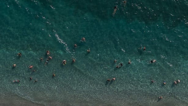 An aerial view shows beachgoers gathered beneath rows of sun umbrellas along the coast of Kanali, in the Preveza region of Greece.