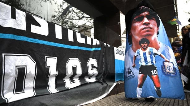 A fan of late Argentine football legend Diego Maradona is wrapped in a flag bearing images of him outside the courthouse during a hearing in the trial into his death, in San Isidro, Buenos Aires province, Argentina, on June 9, 2026