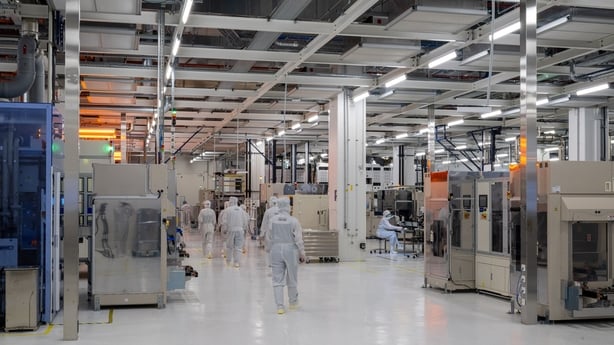Employees in white overalls walk through a production facility