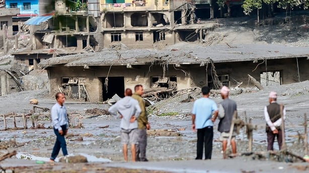 people stand amongst sludge and debris after flash flooding