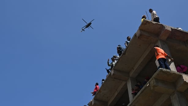 People gather over a building as a rescue helicopter flies past