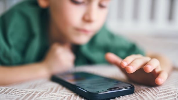 Young boy lying down, reaching for a smartphone on a textured blanket