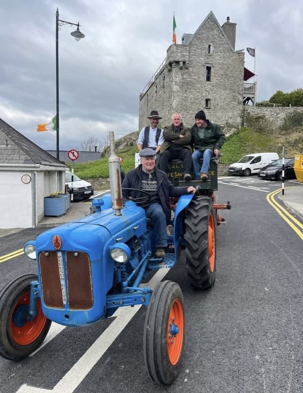 Man driving a blue tractor towing the rocket car