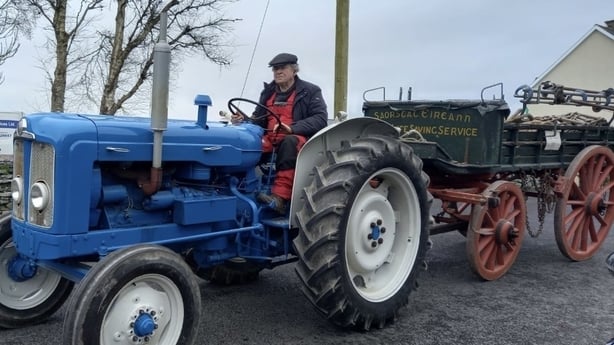 Man driving a blue tractor towing the rocket car