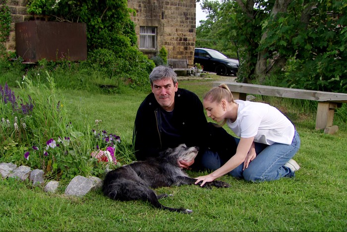 04_08_emm_cain_monty Belle and Cain stand over Monty, who is lay on Zak's grave, in a scene from Emmerdale