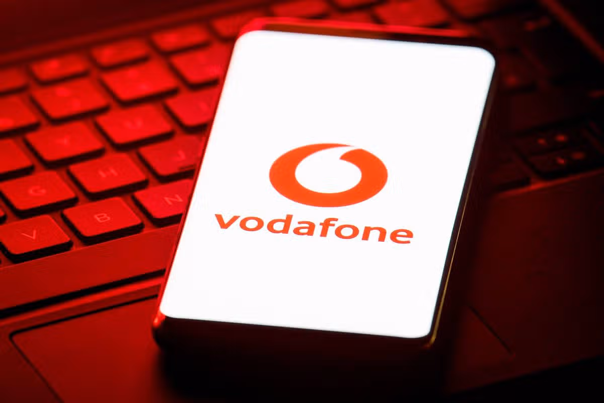 An image showcasing a smartphone with the Vodafone logo displayed prominently on its screen, positioned on a red keyboard with backlighting.