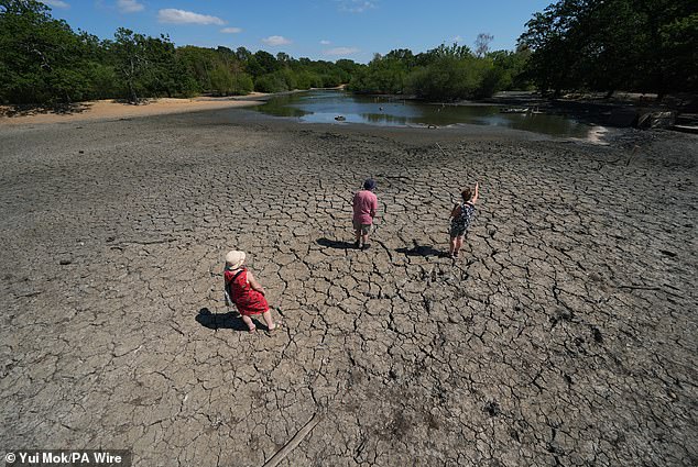 People stand on the exposed, cracked and dried mud bed of Hollow Pond in east London today