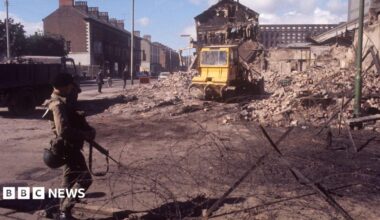 A soldier at a barbed wire barrier amid devastation in Falls Road, Belfast