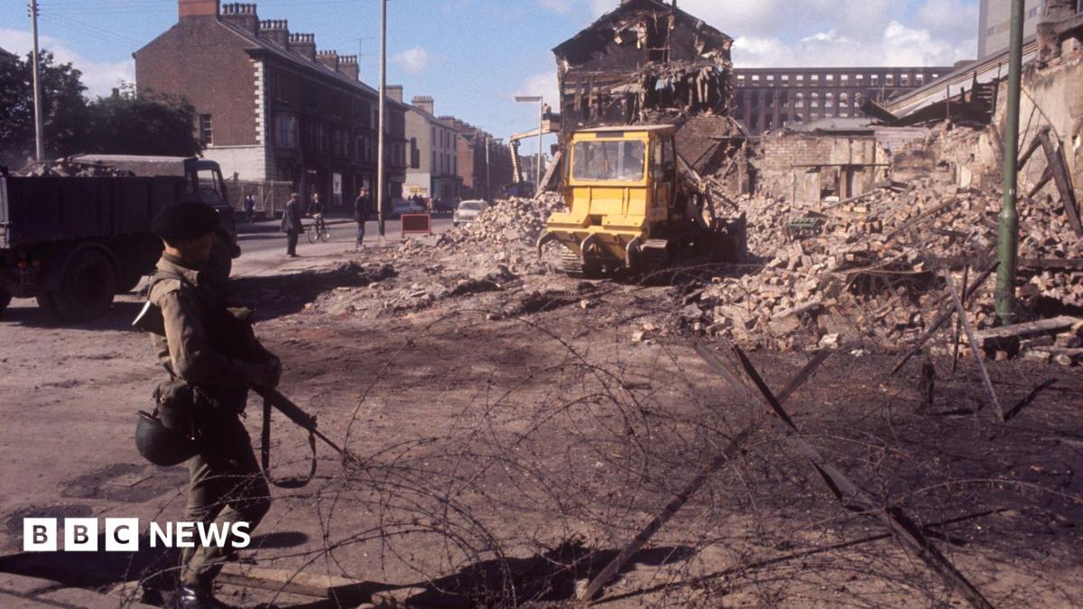 A soldier at a barbed wire barrier amid devastation in Falls Road, Belfast