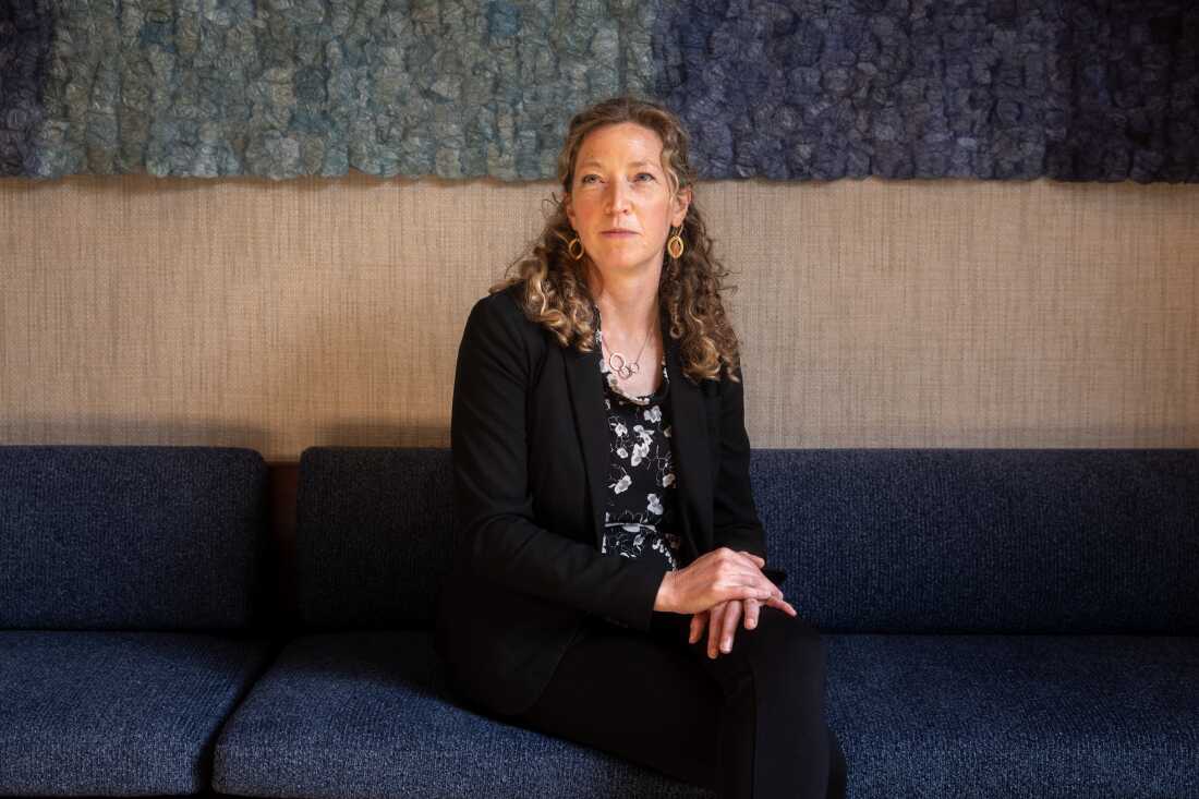 Noella Sudbury is the founder of Rasa Legal, a non-profit that uses technology to help people expunge their criminal records. She is sitting on a couch with her hands in her lap. Sudbury has long, curly hair and she is wearing a dark suit and a dark floral top.