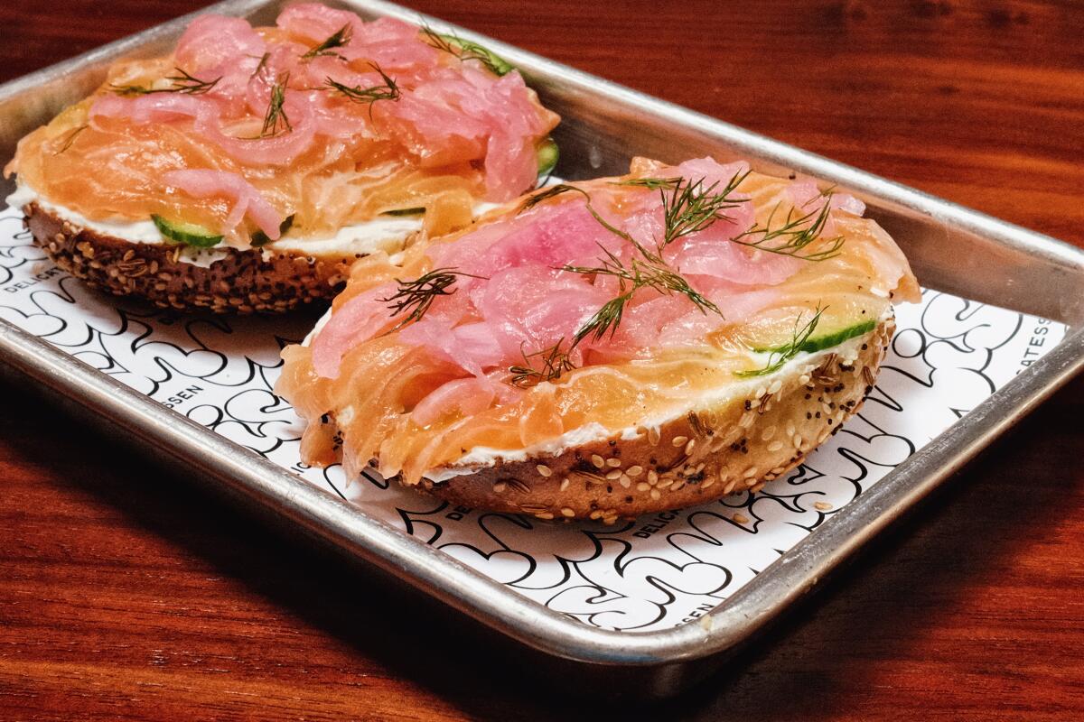 Two everything bagel halves topped with gravlax, cream cheese, pickled red onion and Persian cucumber on a wood table