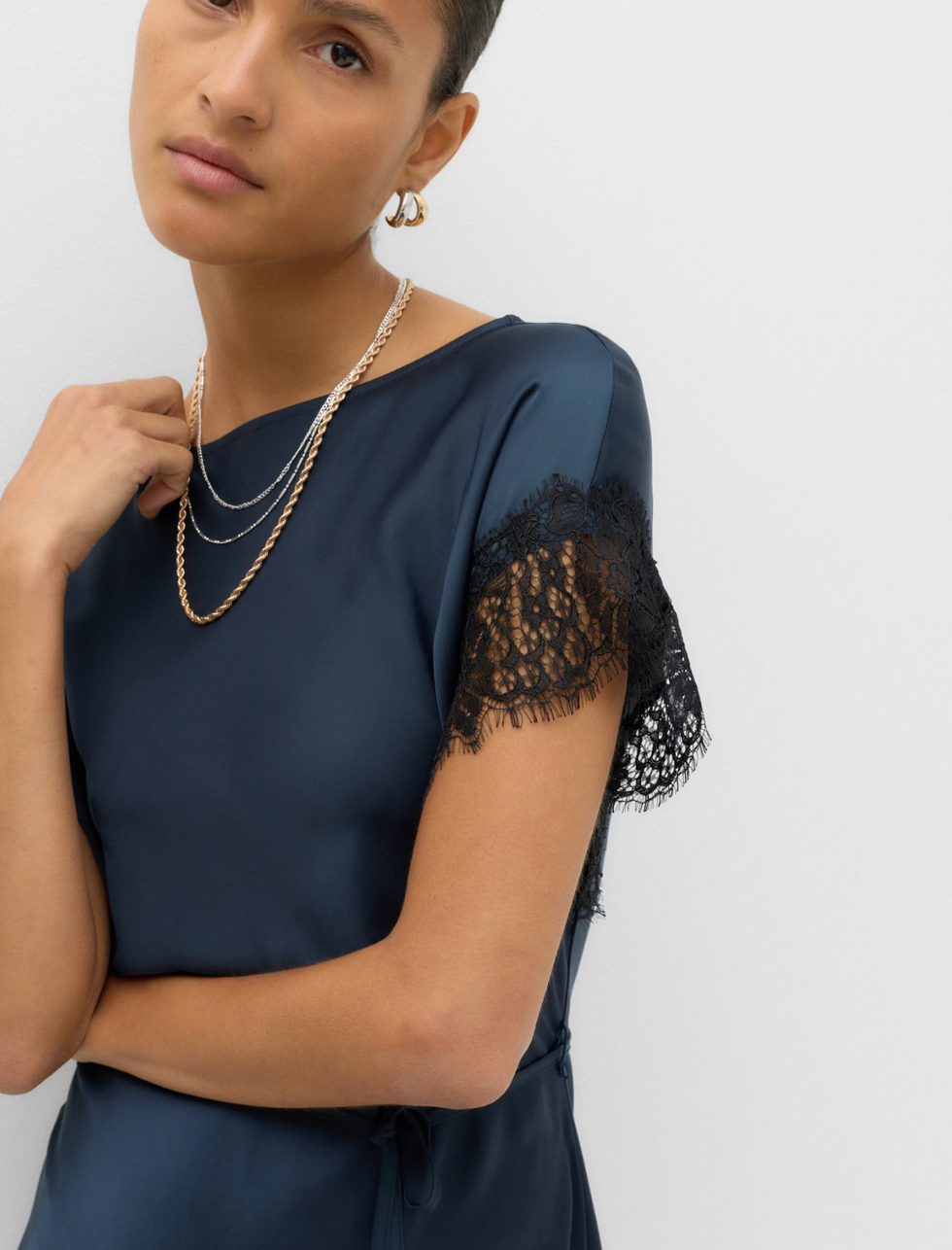 person wearing navy dress with lace sleeves and layered gold necklaces. person wearing navy dress with lace sleeves and layered gold necklaces.