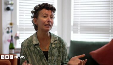 Woman with short brown curly hair wearing a green shirt.
