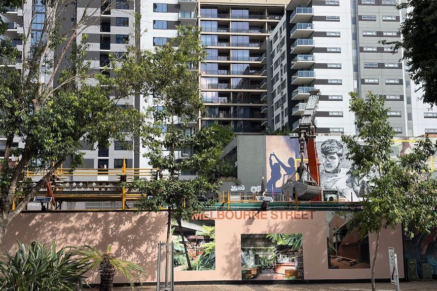 A fence with renders of an apartment building with construction visible in the background.