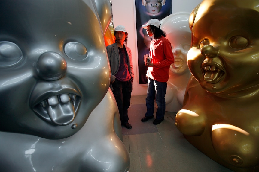 Two men stand behind a large gold and silver sculpture of Mao Zedong.
