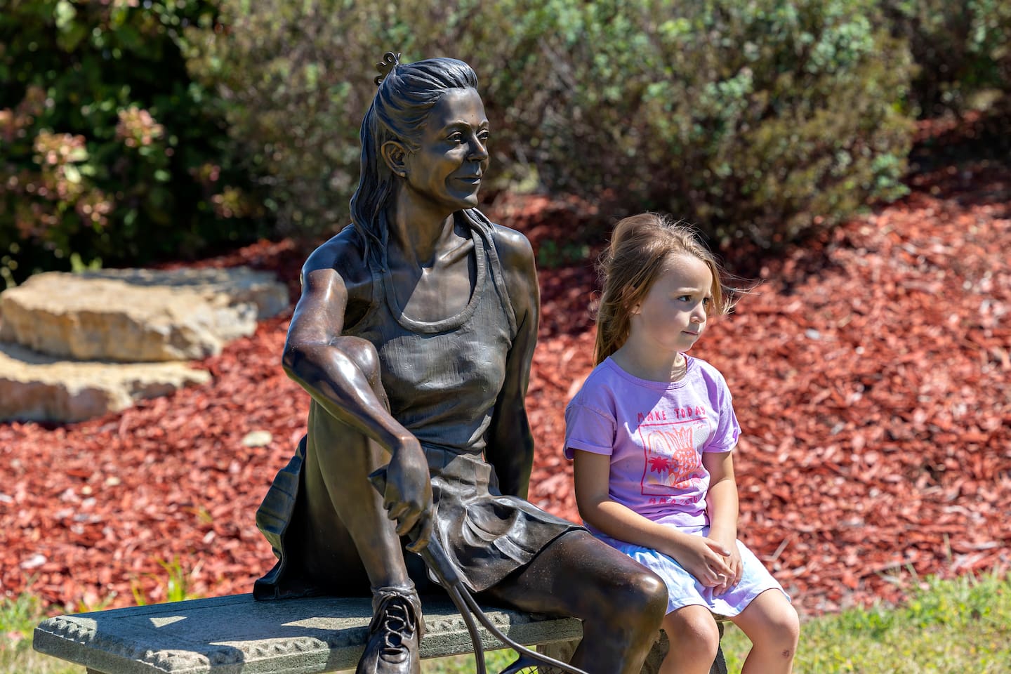Sylvia Sobottka, 4, sits with “Forty Love,” a new sculpture by James Haire put on display Saturday, August 23, 2025, in Rock Falls. Rock Falls Tourism held their annual Art in the Park sculpture walk at RB&W Park.