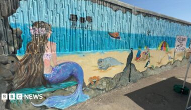 A seafront mural featuring a mermaid, seal, crab, boat and children playing in sand.