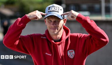 James McClean in a Derry City tracksuit pointing at his baseball cap