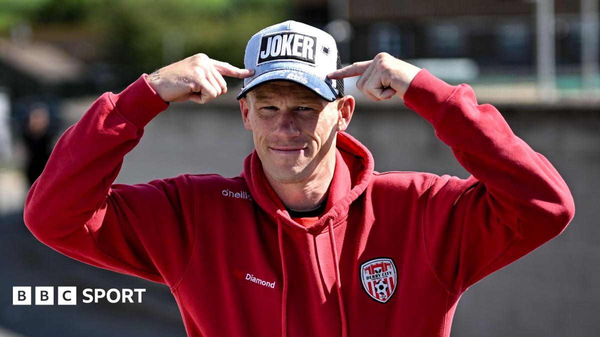 James McClean in a Derry City tracksuit pointing at his baseball cap