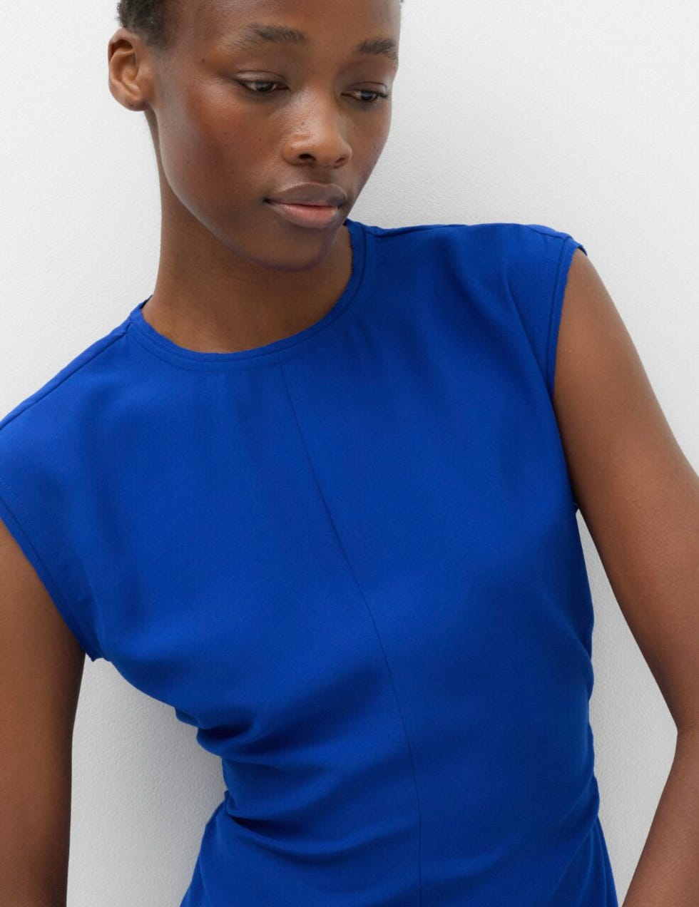 M&S dress person wearing a blue sleeveless top, looking down.
