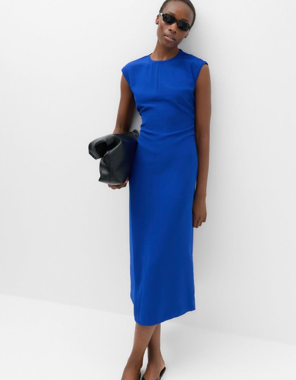 M&S dress person wearing a blue sleeveless dress with black sunglasses, holding a black clutch bag.