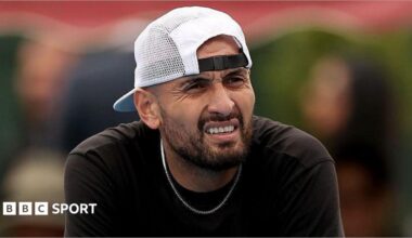 Nick Kyrgios, wearing a baseball cap backwards, looks out while slightly squinting