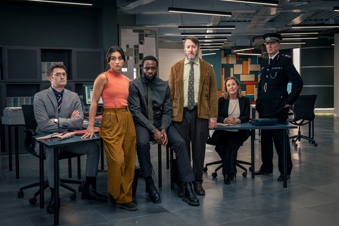 562854,TITLE:Ludwig - Series 2 Ben Ashenden as DS Ethan Cole, Rumi Sutton as DC Caitlin Sullivan, Dipo Ola as DI Russell Carter, David Mitchell as John Ludwig Taylor, Dorothy Atkinson as DCS Carol Shaw and Ralph Ineson as Chief Constable Ziegler in Ludwig, stood sat and leaning in a police office.