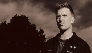 A sepia portrait of Josh Homme in a field next to a tree