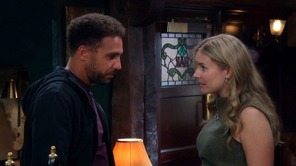 emmerdale billy dawn fletcher two people conversing in a dimly lit room near a stained glass door.
