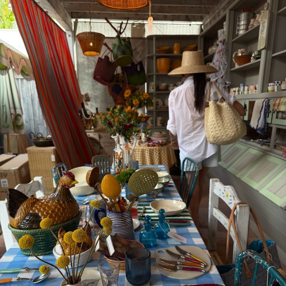 A colorful table setting with stylish dishes, glassware, and a woman with a straw hat in a vintage decor shop.