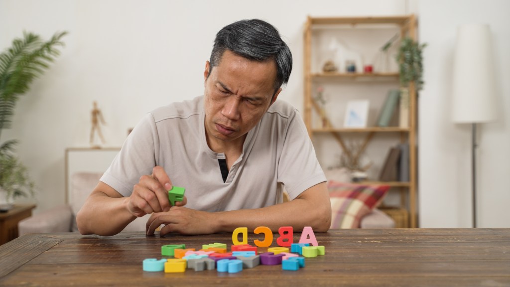 Asian senior man with dementia trying to arrange colored letter blocks in order as brain exercise.
