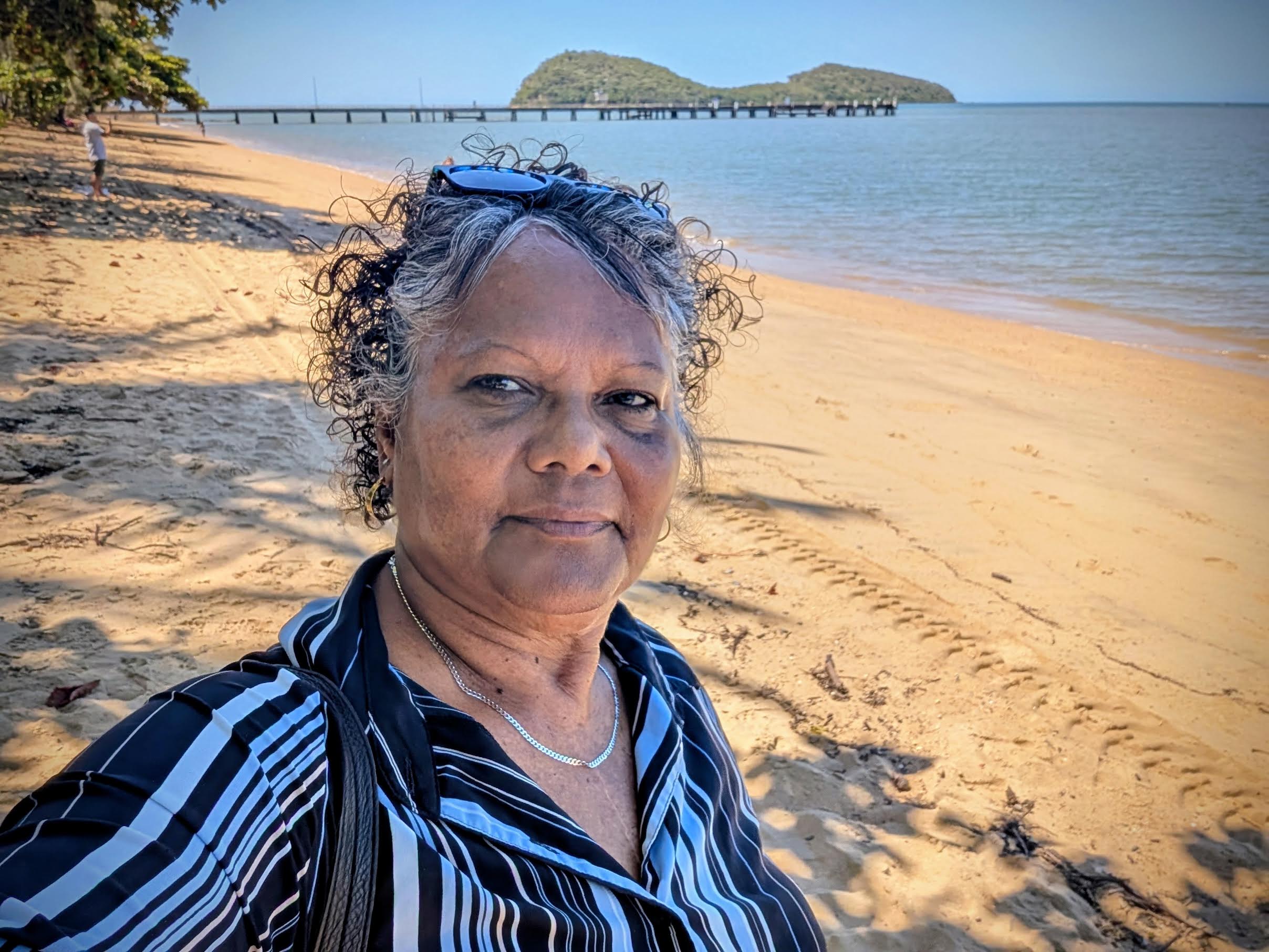 Dr. Mercy Singleton, Director of Research and Engagement Services, Dawul Wuru Aboriginal Corporation, is standing on Palm Cove beach North of Cairns city. It is the traditional home Djikul, of coastal Yirrgandji tribe. The Island in the back is Wangal Djangal or Double Island. Image courtesy of Dr. Mercy Singleton.