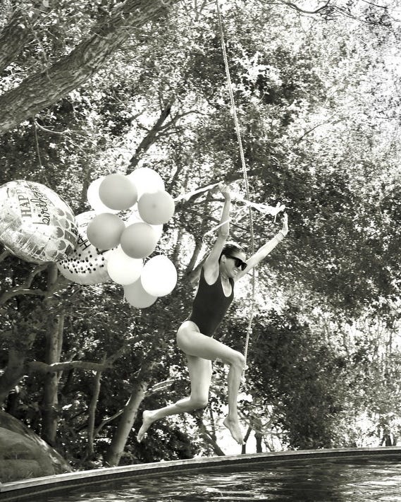 meghan markle jumps into a pool while holding colorful balloons and celebrating a birthday.