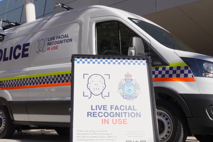 A sign reading live facial recognition in use in front of a police van.