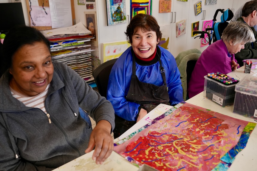 Two people smiling while seated an an art-making table.