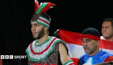Prichard Colon wears a sparkly red, silver and green vest and headband with feathers