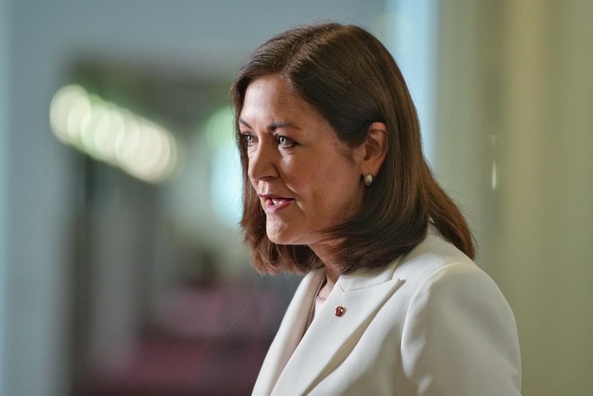 A woman in a white suit talks to media.