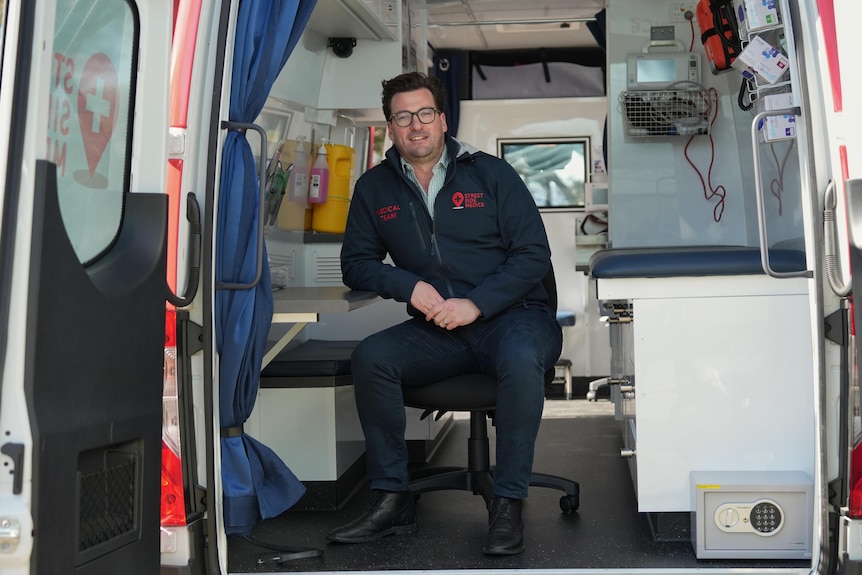 A man sits inside a medical van looking at the camera.